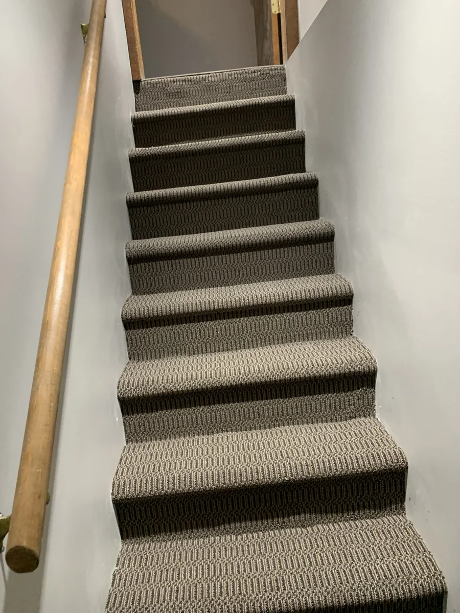 Gray carpet steps with clean wrapped edges and wood handrail